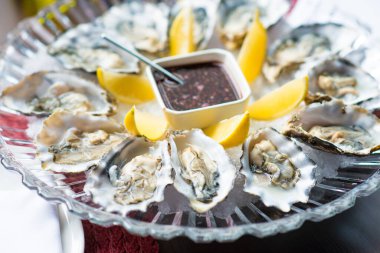 Yuvarlak tabakta limonlu taze istiridye. İstiridye sezonu. Mavi arka planda deniz ürünleri tabağı. Yarım kabuklu istiridye..