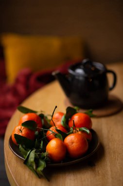 Tahta bir masada yeşil yapraklı taze mandalinalar. Mandalina ve çaydanlık, kır tarzında çay.