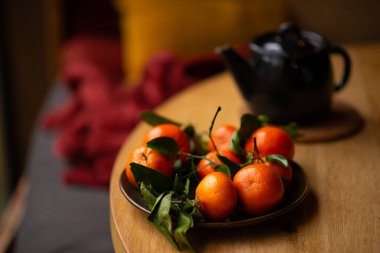 Tahta bir masada yeşil yapraklı taze mandalinalar. Mandalina ve çaydanlık, kır tarzında çay.