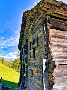 Ahşap duvarları ve zemini olan eski bir sepet dokuma atölyesinin içinde, pencerelerin altında çeşitli dokuma malzemeler var.