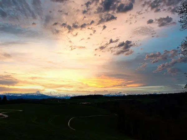 stock image Stunning sunset over a lush Swiss landscape, featuring a winding