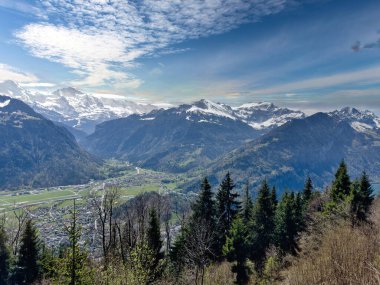 Karla kaplı dağlarla kaplı bir vadinin panoramik manzarası ve parçalı bulutlu bir gökyüzü.