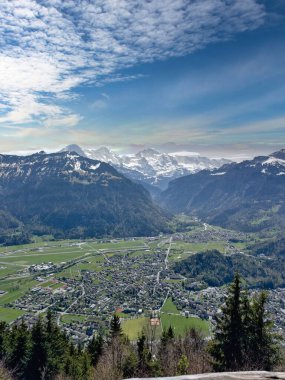Karla kaplı dağlarla kaplı bir vadinin panoramik manzarası ve parçalı bulutlu bir gökyüzü.