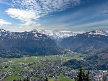 Karla kaplı dağlarla kaplı bir vadinin panoramik manzarası ve parçalı bulutlu bir gökyüzü.