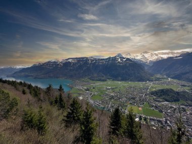 Geleneksel bir binası ve gün batımında karla kaplı dağları olan bir tepenin yanındaki göl kenti manzarası.