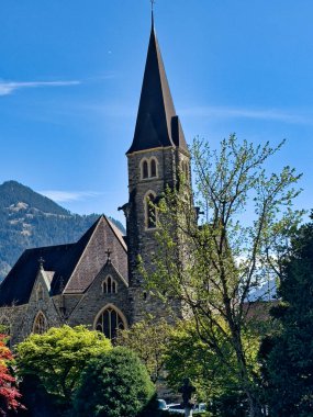 Gökyüzünde parlak kırmızı yaprakları ve evleri olan ağaç dalları tarafından çerçevelenmiş bir kilise kulesinin manzarası.