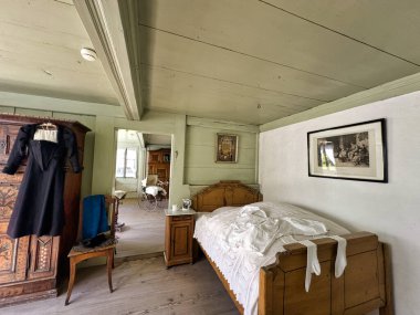 Geleneksel bir yatak odası. Antik ahşap mobilyalar. Detaylı bir gardırop ve beyaz örtülü bir yatak.