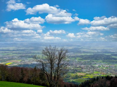 Bereketli bir vadinin panoramik manzarası kıvrımlı bir nehir, yeşil tarlalar, ve parçalı bulutlu mavi bir gökyüzü, bir yamaçtan görünen ağaçlarla ön planda