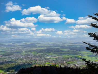 Bereketli bir vadinin panoramik manzarası kıvrımlı bir nehir, yeşil tarlalar, ve parçalı bulutlu mavi bir gökyüzü, bir yamaçtan görünen ağaçlarla ön planda