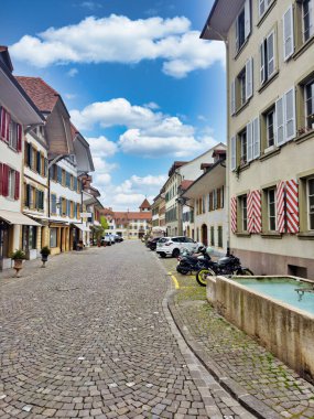Kırmızı kiremitli çatıları, kilise kulesi ve parçalı bulutlu gökyüzü altında iyi korunmuş bahçeleri olan büyüleyici bir ortaçağ kasabasının havadan görünüşü.