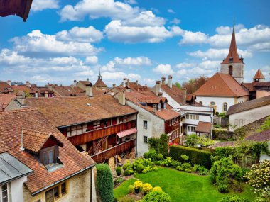 Kırmızı kiremitli çatıları, kilise kulesi ve parçalı bulutlu gökyüzü altında iyi korunmuş bahçeleri olan büyüleyici bir ortaçağ kasabasının havadan görünüşü.