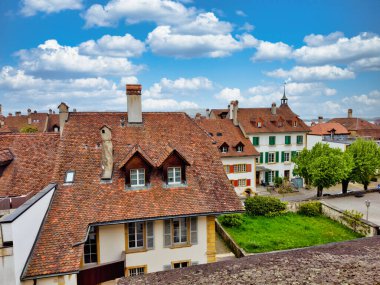 Kırmızı kiremitli çatıları, kilise kulesi ve parçalı bulutlu gökyüzü altında iyi korunmuş bahçeleri olan büyüleyici bir ortaçağ kasabasının havadan görünüşü.