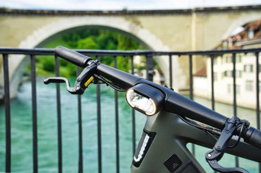 Tarihi köprüsü ve arka planında binaları olan nehre bakan taştan bir terasa park edilmiş modern elektrikli bisiklet.