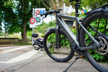 Arka planda geleneksel evler olan, yapraklı bir mahallede kaldırıma park etmiş, pannier çantalı modern elektrikli bisiklet.