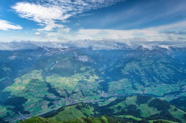 Dağlarla ve vadilerle çevrili, parçalı bulutlu mavi gökyüzünün altında dağınık köylerle panoramik bir göl manzarası.