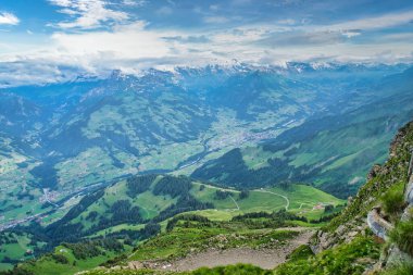 Dağlarla ve vadilerle çevrili, parçalı bulutlu mavi gökyüzünün altında dağınık köylerle panoramik bir göl manzarası.