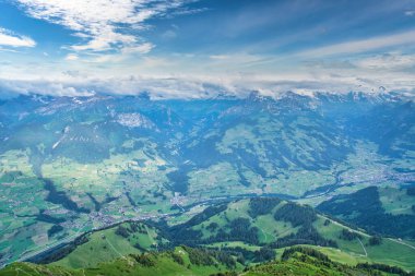 Dağlarla ve vadilerle çevrili, parçalı bulutlu mavi gökyüzünün altında dağınık köylerle panoramik bir göl manzarası.
