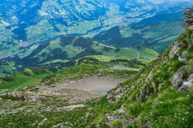 Dağlarla ve vadilerle çevrili, parçalı bulutlu mavi gökyüzünün altında dağınık köylerle panoramik bir göl manzarası.