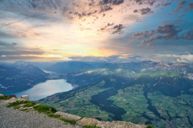 Gün batımında, dramatik bulutlar ve vadilerle çevrili, İsviçre bayrağı ve dağ kulübesinde nefes kesici bir dağ zirvesi.