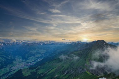 Gün batımında yeşil dağların ve vadilerin büyüleyici manzarası. Dağa çıkan dolambaçlı bir patika ve gökyüzündeki dramatik bulutlar.