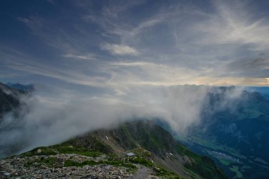 Gün batımında yeşil dağların ve vadilerin büyüleyici manzarası. Dağa çıkan dolambaçlı bir patika ve gökyüzündeki dramatik bulutlar.