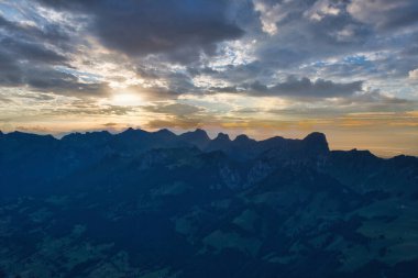Gün batımında renkli gökyüzü ve bulutlarla dağ siluetlerinin dramatik manzarası