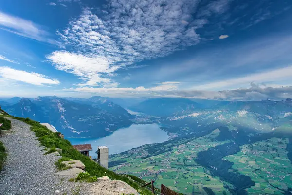 Dağlarla ve vadilerle çevrili, parçalı bulutlu mavi gökyüzünün altında dağınık köylerle panoramik bir göl manzarası.