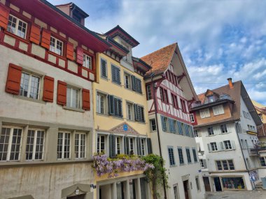 Tarihi binaları ve renkli mimarisi olan bir Avrupa şehrinde rahat bir cadde. Sahnede ön planda dekoratif bir çeşme ve eski evlerin büyüleyici cepheleri yer alıyor..