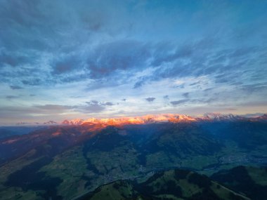 Alacakaranlıktaki bir dağ sırasının çarpıcı manzarası. Tepeler batan güneşten gelen sıcak, altın bir ışıkla yıkanmış. Gökyüzü mavi ve turuncu renklerin bir karışımıdır, aşağıdaki engebeli araziye karşı güzel bir kontrastlık yaratır.