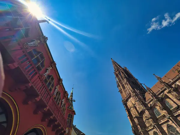 stock image Gothic-style architecture with intricate details and a prominent spire under a clear blue sky. The sun adds a bright highlight to the scene, enhancing the vibrant colors of the buildings