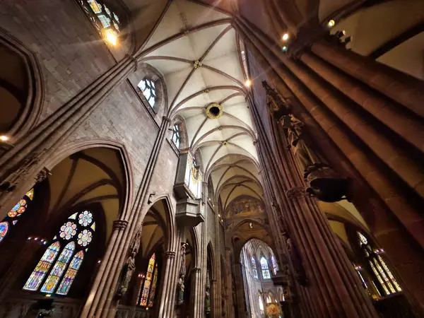 stock image Interior of a grand Gothic-style cathedral with high arches, stained glass windows, and an ornate organ. The light streaming through the windows creates a serene and spiritual atmosphere