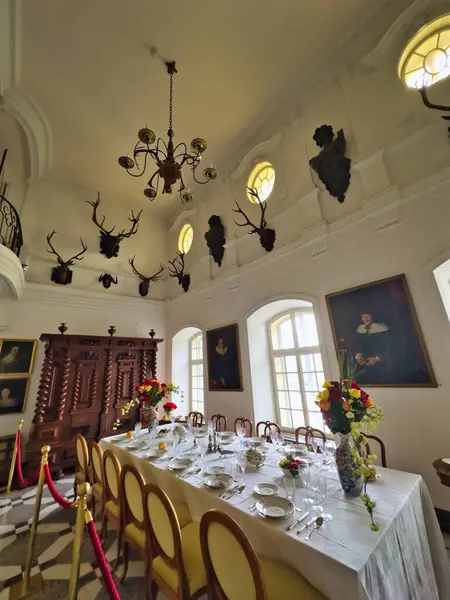 stock image A stately dining room with high ceilings, featuring a long, elegantly set table. The walls are adorned with portraits and mounted deer antlers, creating a sophisticated and grand atmosphere