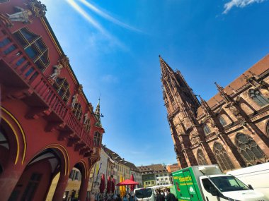 13.07.24.Germany. Gothic-style architecture with intricate details and a prominent spire under a clear blue sky. The sun adds a bright highlight to the scene, enhancing the vibrant colors of the buildings clipart