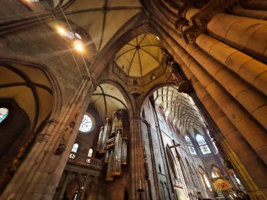 13.07.24 Alman. Yüksek kemerli, vitray pencereli ve süslü bir organı olan Gotik tarzı büyük bir katedralin içi. Camlardan süzülen ışık dingin ve ruhsal bir atmosfer yaratıyor.