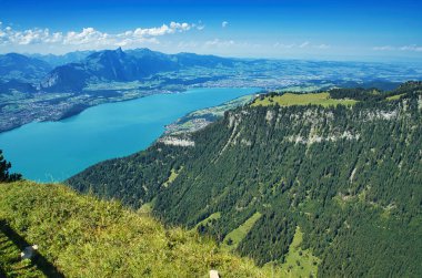 Vadisi olan bir dağ manzarası, yeşil tepeler ve arka planda mavi bir gökyüzü.
