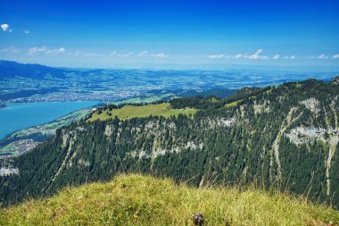 Vadisi olan bir dağ manzarası, yeşil tepeler ve arka planda mavi bir gökyüzü.