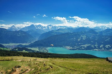 Sersemletici bir dağ manzarasının üzerinde süzülen bir paraglider, açık mavi gökyüzünün altında karla kaplı tepeler ve derin vadilerle