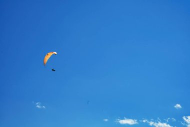 Sersemletici bir dağ manzarasının üzerinde süzülen bir paraglider, açık mavi gökyüzünün altında karla kaplı tepeler ve derin vadilerle
