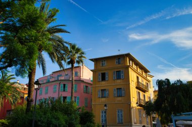 Yat ve teknelerle dolu hareketli bir liman, parçalı bulutlu bir gökyüzünün altındaki renkli tepe binalarının zeminine kurulmuş.