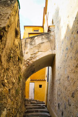 Açık mavi gökyüzü altında karmaşık mimari detaylara sahip tarihi binaları gösteren bir sokak manzarası.