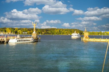 Tekneleri, heykeli ve bulutların altında yemyeşil arka planı olan manzaralı bir liman.