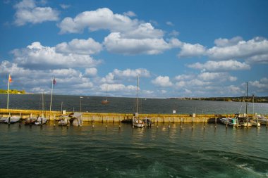 Tekneleri, heykeli ve bulutların altında yemyeşil arka planı olan manzaralı bir liman.