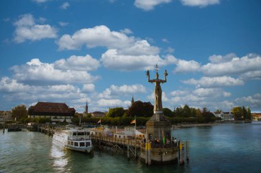 Tekneleri, heykeli ve bulutların altında yemyeşil arka planı olan manzaralı bir liman.