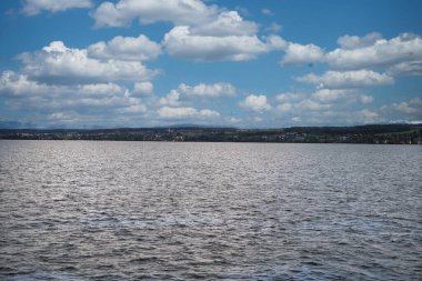 Durgun göl, uzak karla kaplı dağlar, canlı bir gökyüzünün altında.
