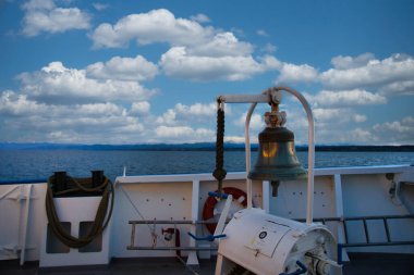 Arka planda dağlar ve göl olan bir geminin çanı.