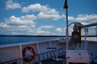 Arka planda dağlar ve göl olan bir geminin çanı.