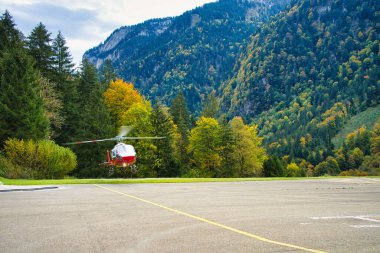 Helikopter bir helikopter pistine park etmiş. Etrafı yemyeşil dağ manzarasıyla çevrili.