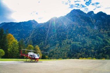 Helikopter bir helikopter pistine park etmiş. Etrafı yemyeşil dağ manzarasıyla çevrili.