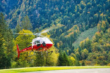 Helikopter bir helikopter pistine park etmiş. Etrafı yemyeşil dağ manzarasıyla çevrili.