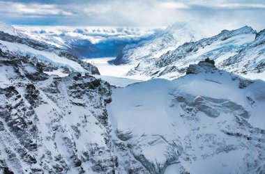 Engebeli zirveleri ve dramatik bulutlu gökyüzü olan görkemli karla kaplı dağlar.